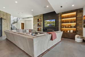 Spacious living area featuring stone accent walls, integrated fireplace with television, recessed and accent lighting, and a contemporary staircase with metal railings