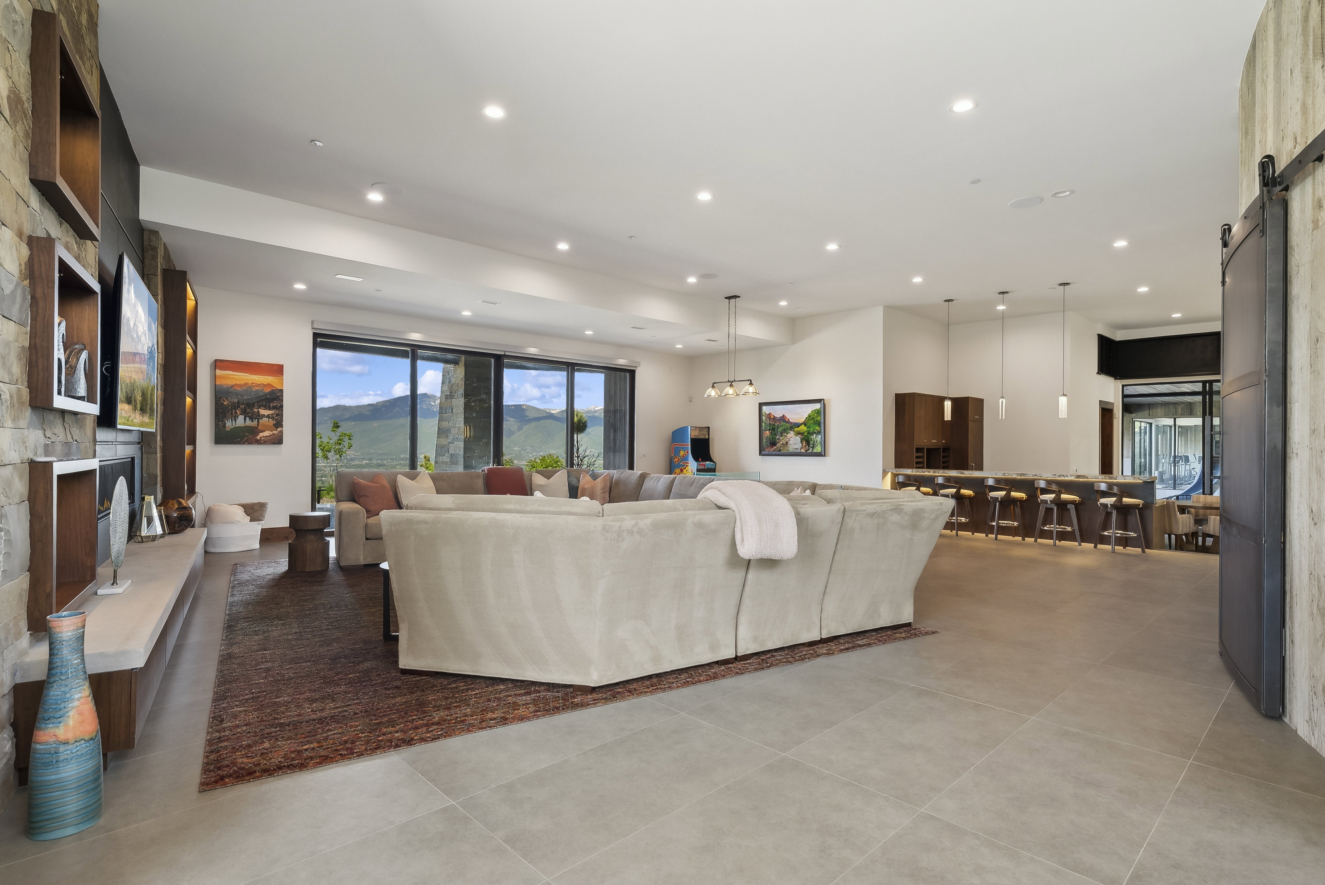 Spacious open-concept living area featuring large format tile flooring, a stone accent wall, and recessed lighting