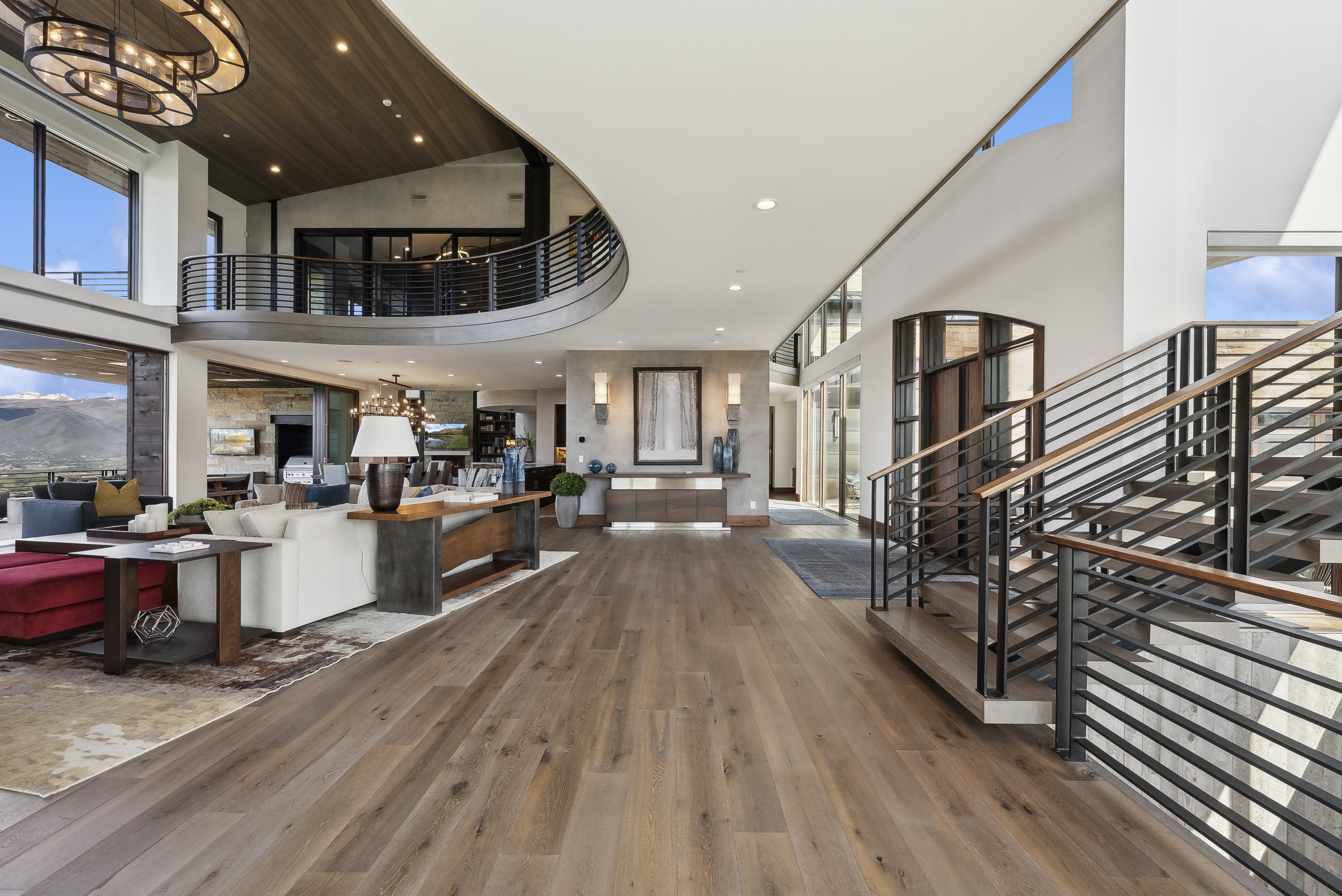 Grand entry hall featuring wide-plank wood-finish flooring, a contemporary staircase with horizontal metal railings, and a curved upper-level balcony