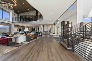 Grand entry hall featuring wide-plank wood-finish flooring, a contemporary staircase with horizontal metal railings, and a curved upper-level balcony