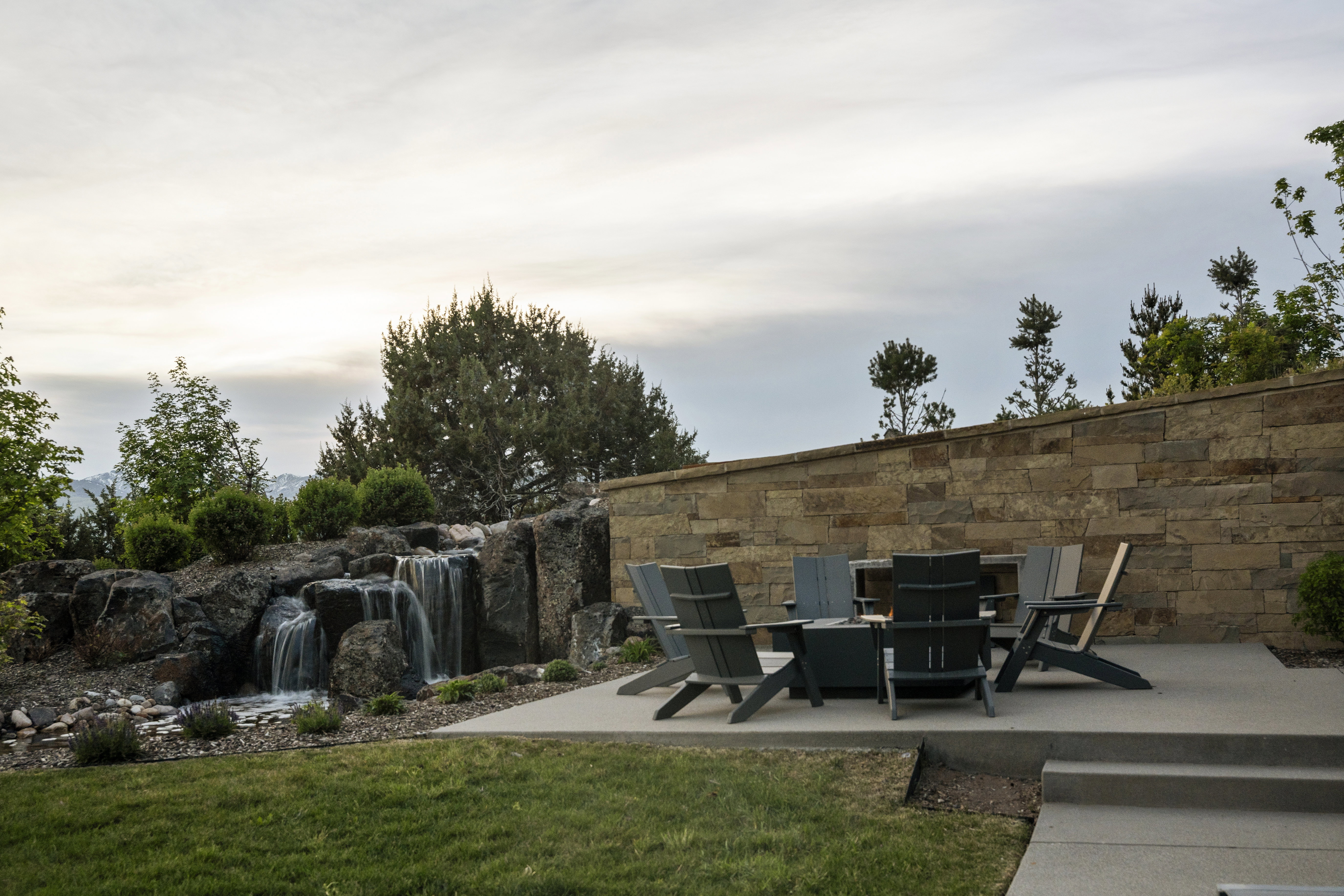 Expansive stone water feature with multiple cascades, surrounded by natural rock landscaping and mature greenery