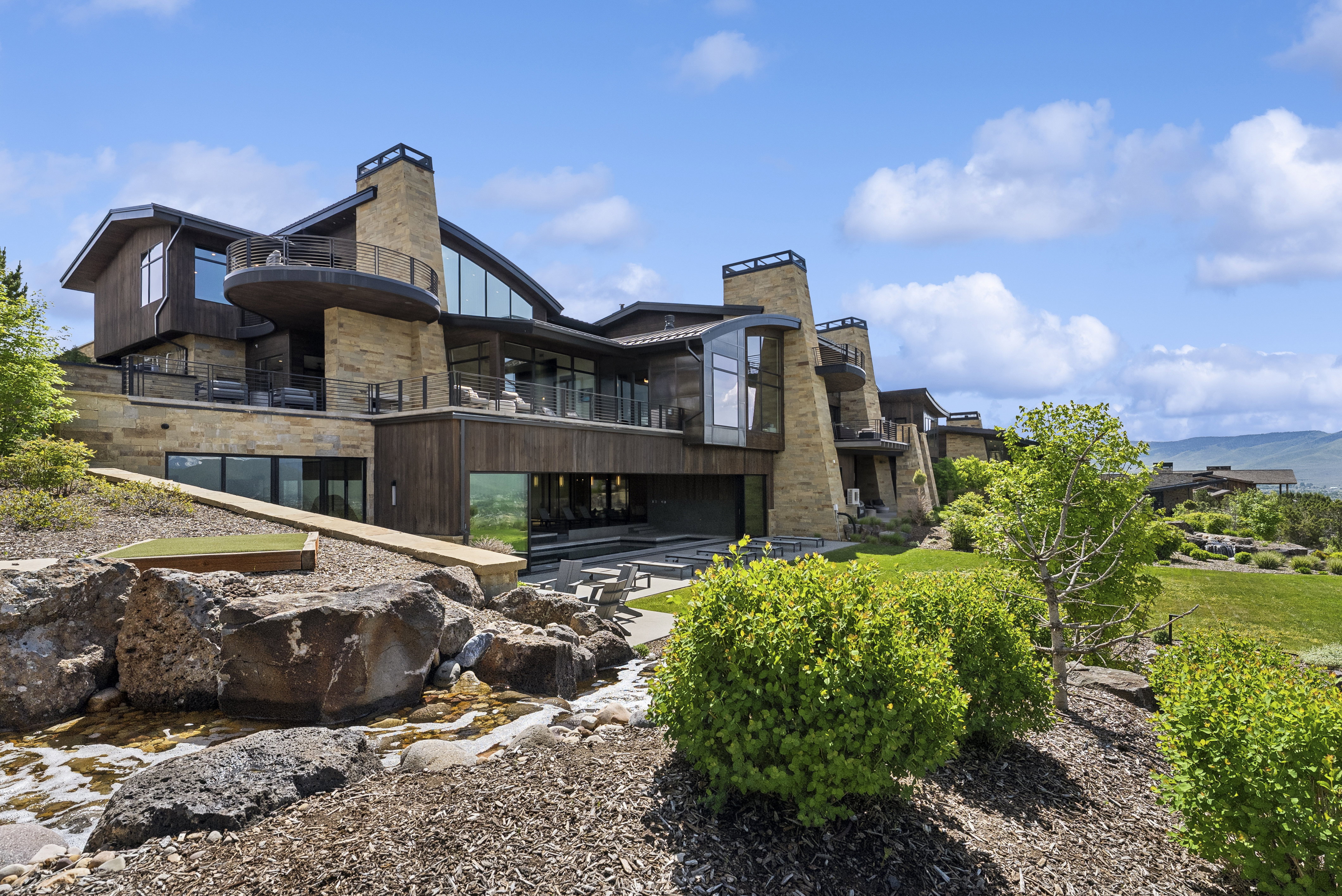 Expansive multi-level residence featuring stone and wood-panel exterior, multiple balconies, and floor-to-ceiling windows