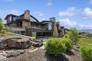 Expansive multi-level residence featuring stone and wood-panel exterior, multiple balconies, and floor-to-ceiling windows