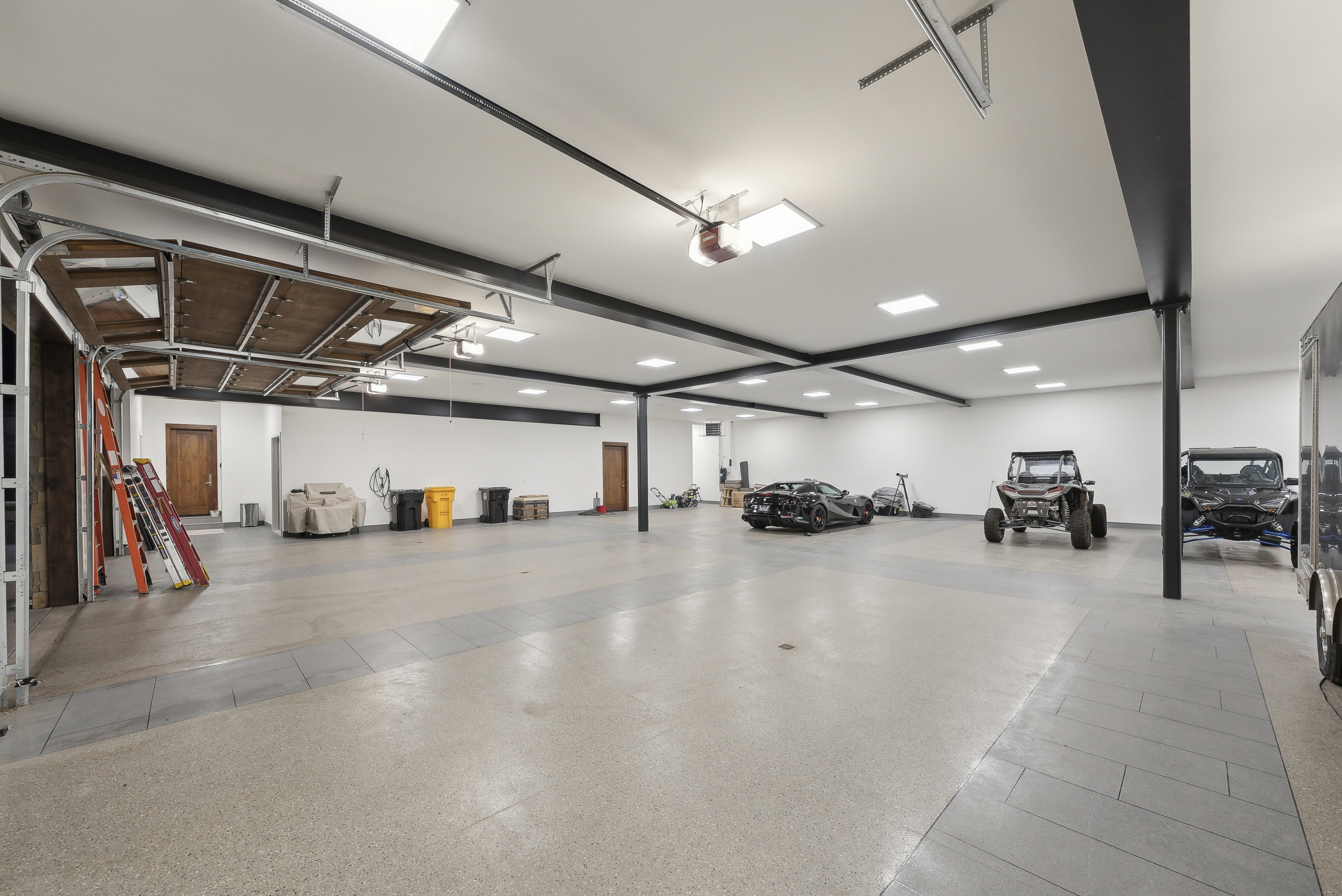 Spacious garage with an epoxy floor finish, multiple skylights, recessed lighting, and exposed black structural beams