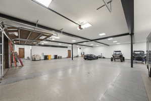 Spacious garage with an epoxy floor finish, multiple skylights, recessed lighting, and exposed black structural beams