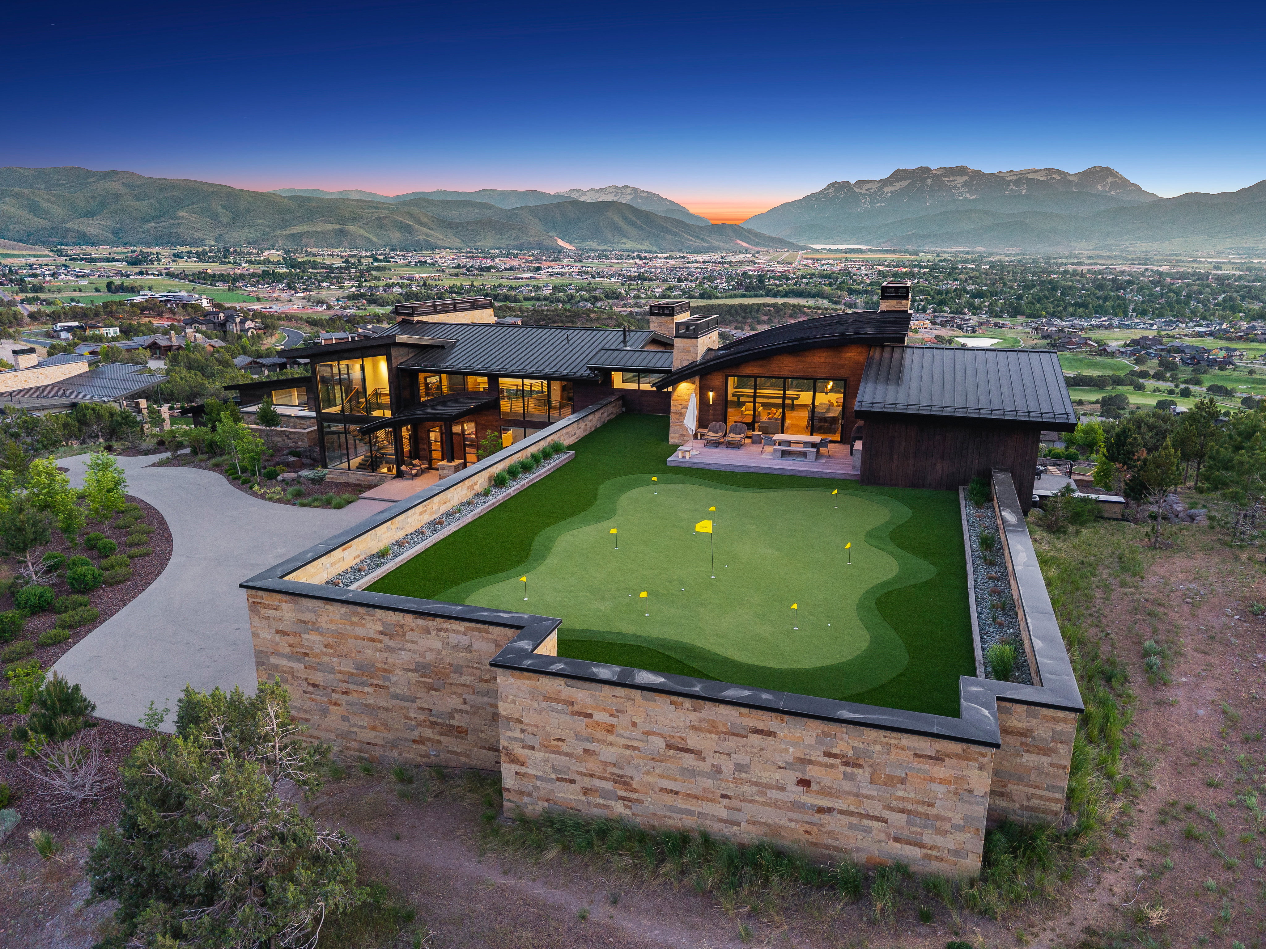 Modern residence featuring extensive glass facades, a private putting green, and stone retaining walls