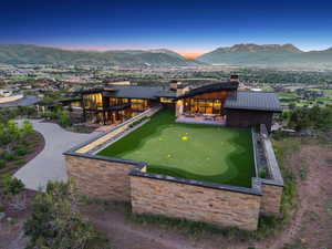 Modern residence featuring extensive glass facades, a private putting green, and stone retaining walls