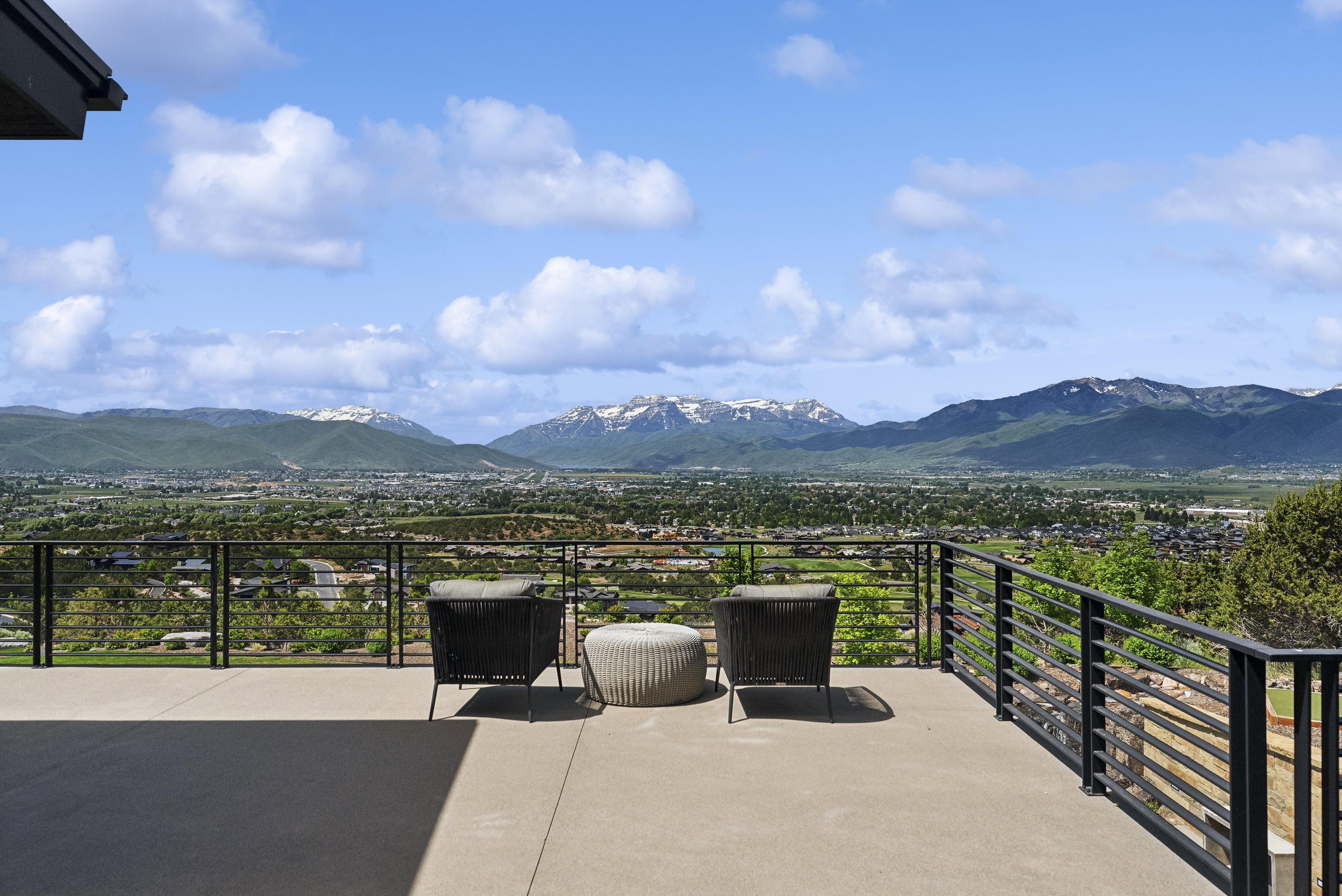 Expansive outdoor patio with concrete flooring, featuring a black horizontal bar railing system and a panoramic mountain landscape