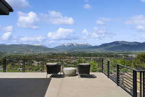 Expansive outdoor patio with concrete flooring, featuring a black horizontal bar railing system and a panoramic mountain landscape