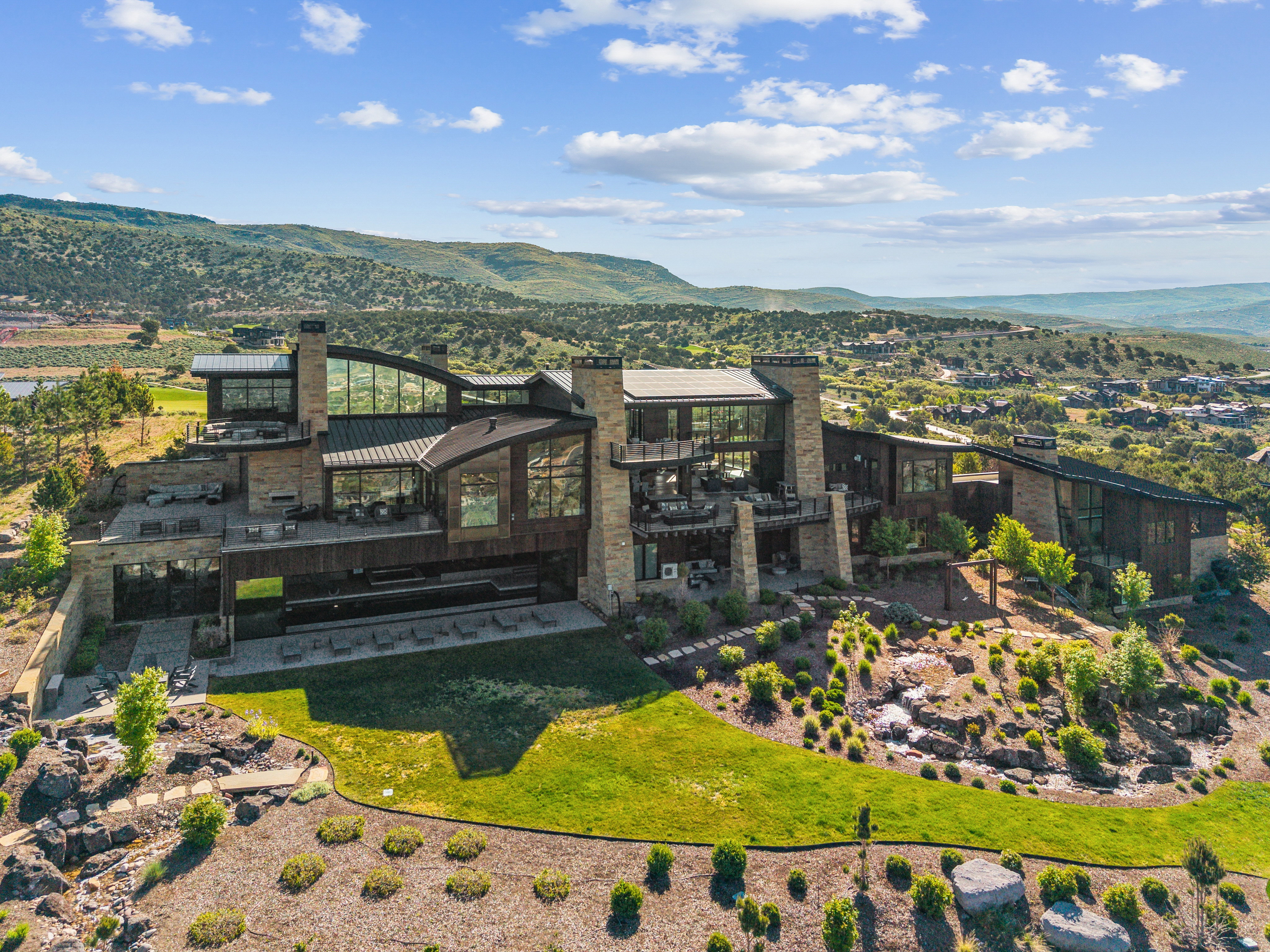 Architectural residence featuring extensive glazing, multiple outdoor terraces, and stone and dark wood-finish cladding