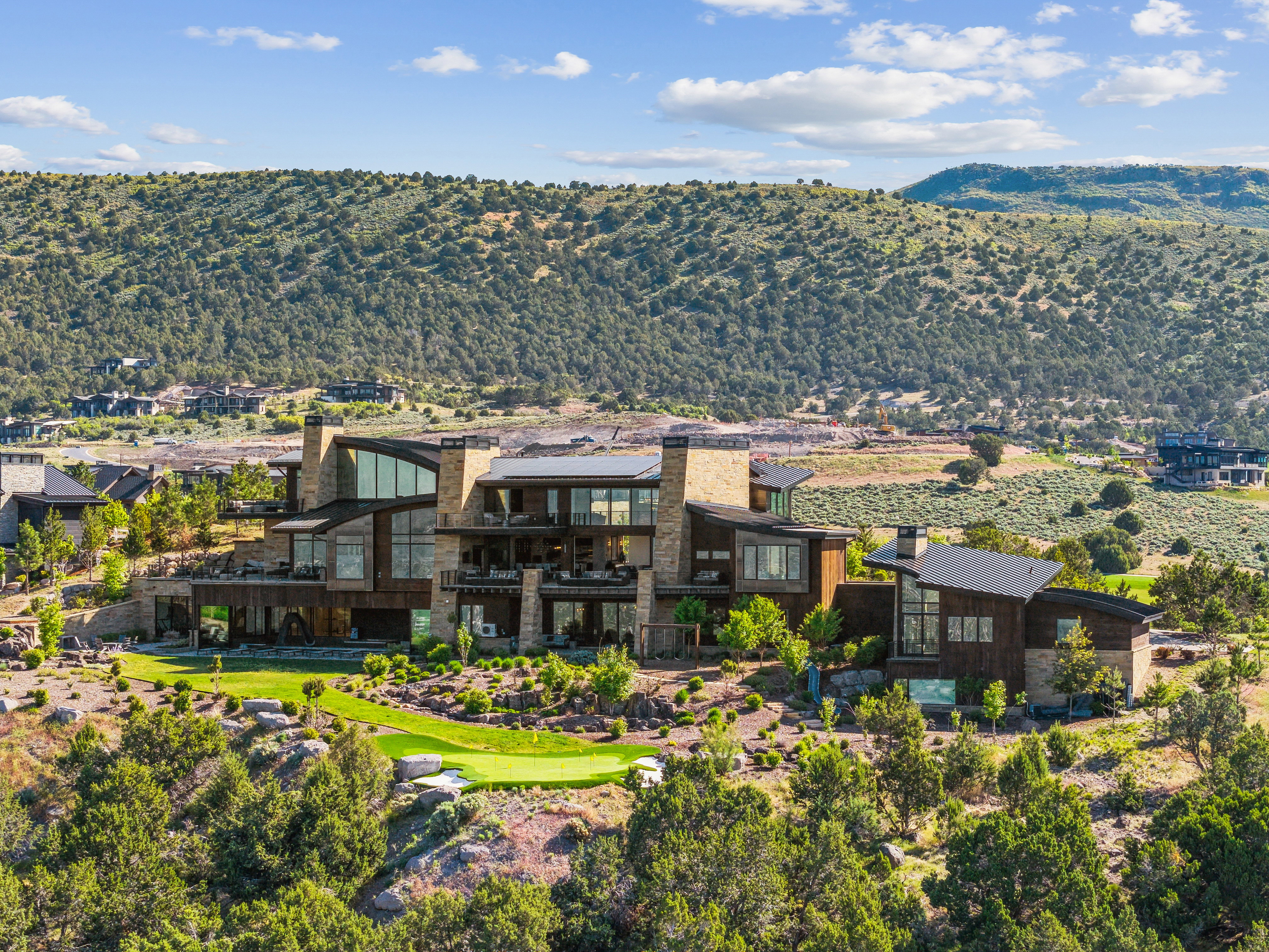 Contemporary mountain residence featuring multiple balconies, expansive glazing, stone and wood-panel exterior finishes, and a manicured putting green