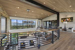 Upper-level landing featuring panoramic windows, a circular metal railing with a wood-finish top, wood-finish flooring, a wood-paneled ceiling with recessed lighting, and exposed steel beams