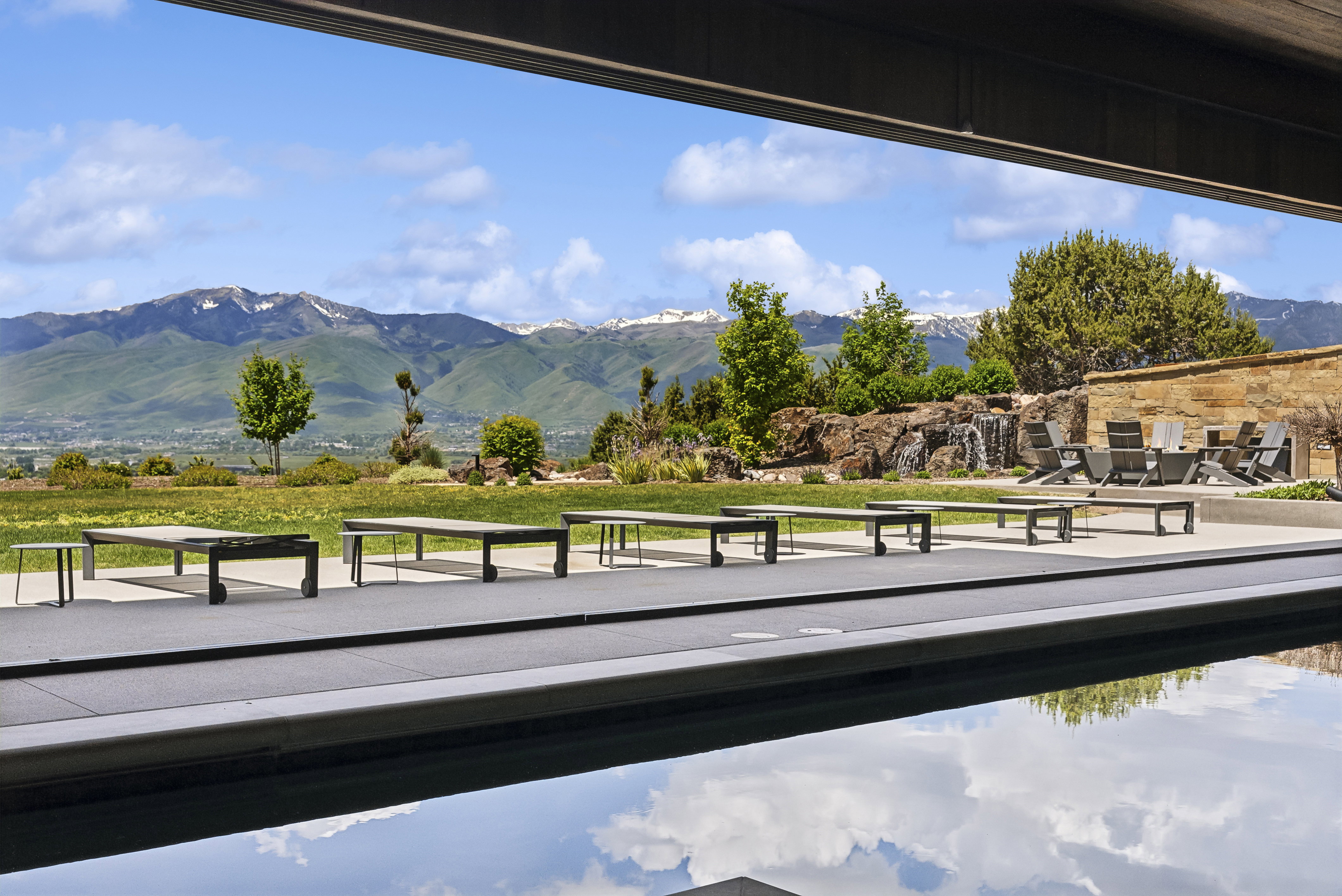 Outdoor entertainment area featuring a dark-tiled pool with a concrete surround, a stone water feature, and a paved patio area