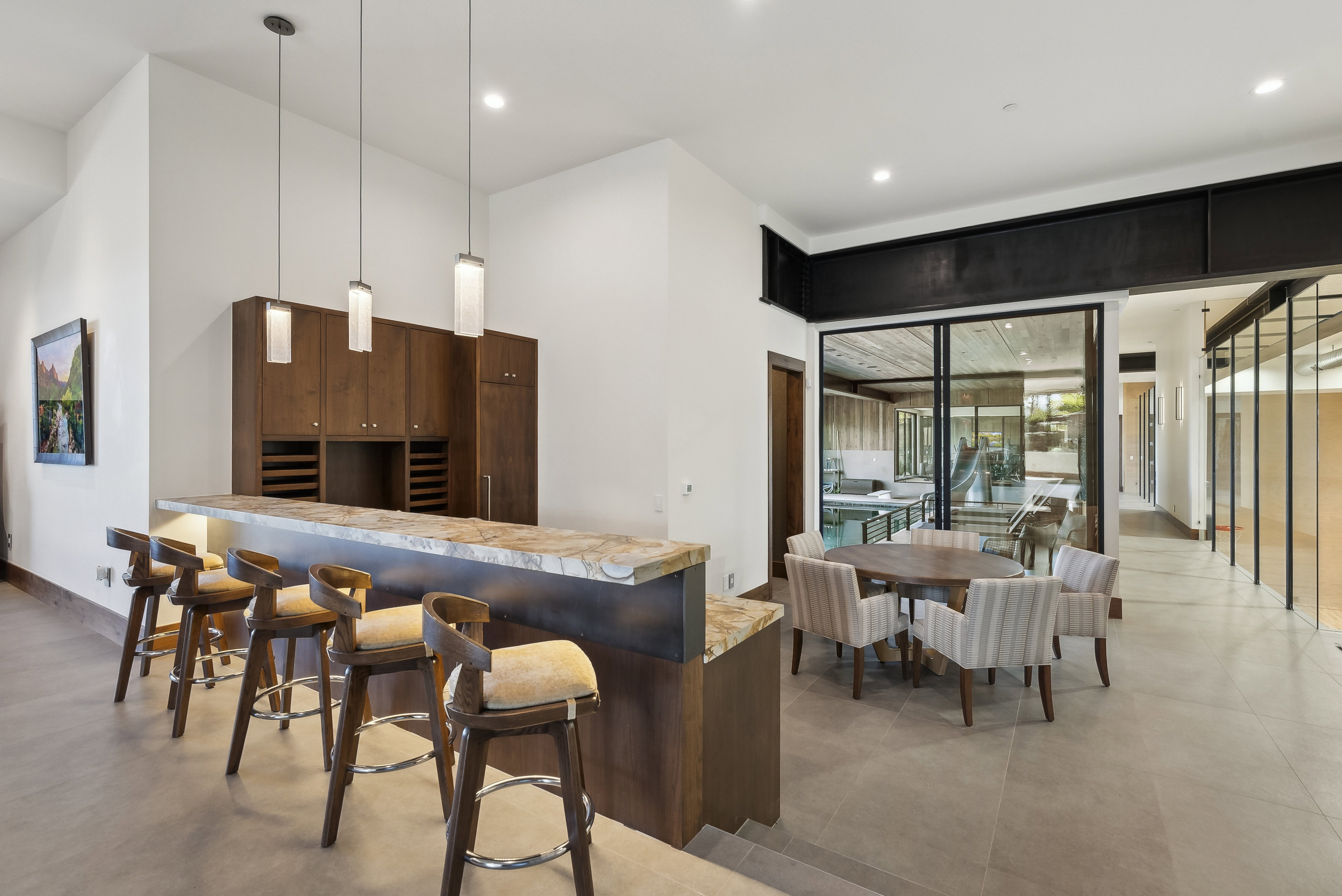 Integrated wet bar featuring a stone countertop, wood cabinetry with wine storage, and three pendant lights