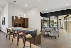 Integrated wet bar featuring a stone countertop, wood cabinetry with wine storage, and three pendant lights