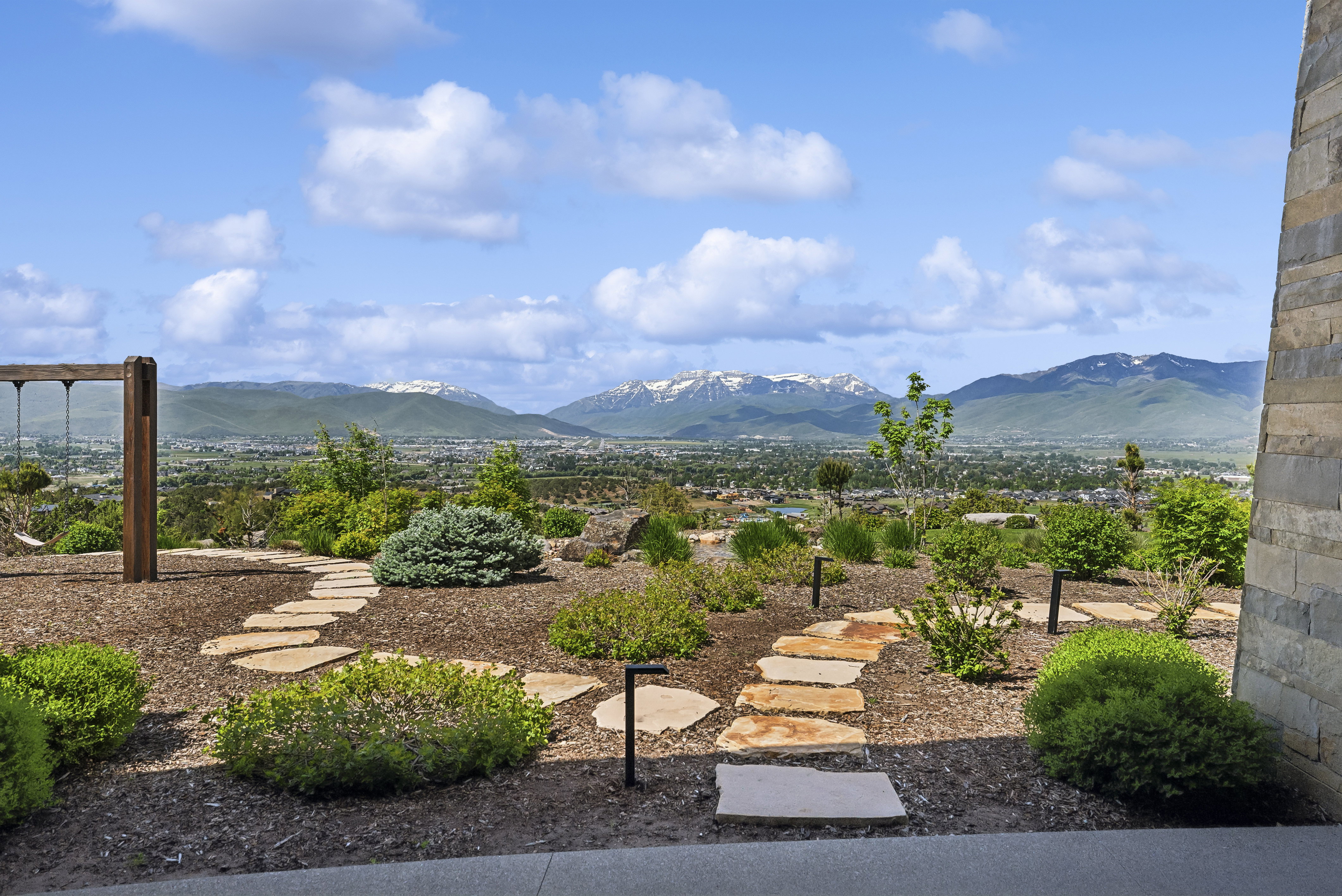 Landscaped outdoor area featuring a natural stone pathway, established plantings, ground-level lighting, and distant mountain scenery
