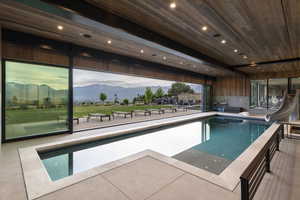 Indoor-outdoor swimming pool featuring retractable glass doors, light-toned tile surround, and a built-in slide