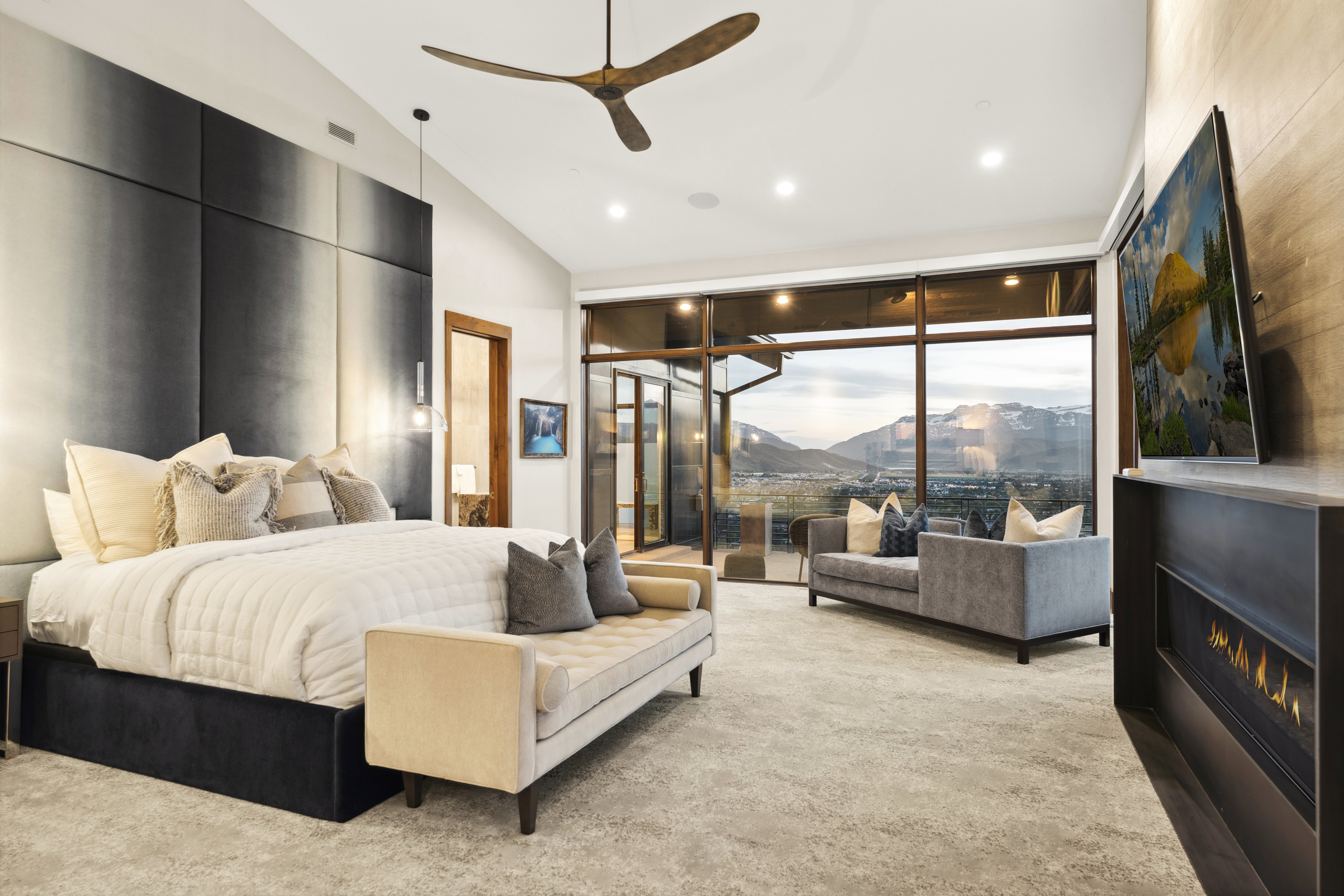 Spacious bedroom featuring floor-to-ceiling windows, a linear fireplace, and a contemporary ceiling fan