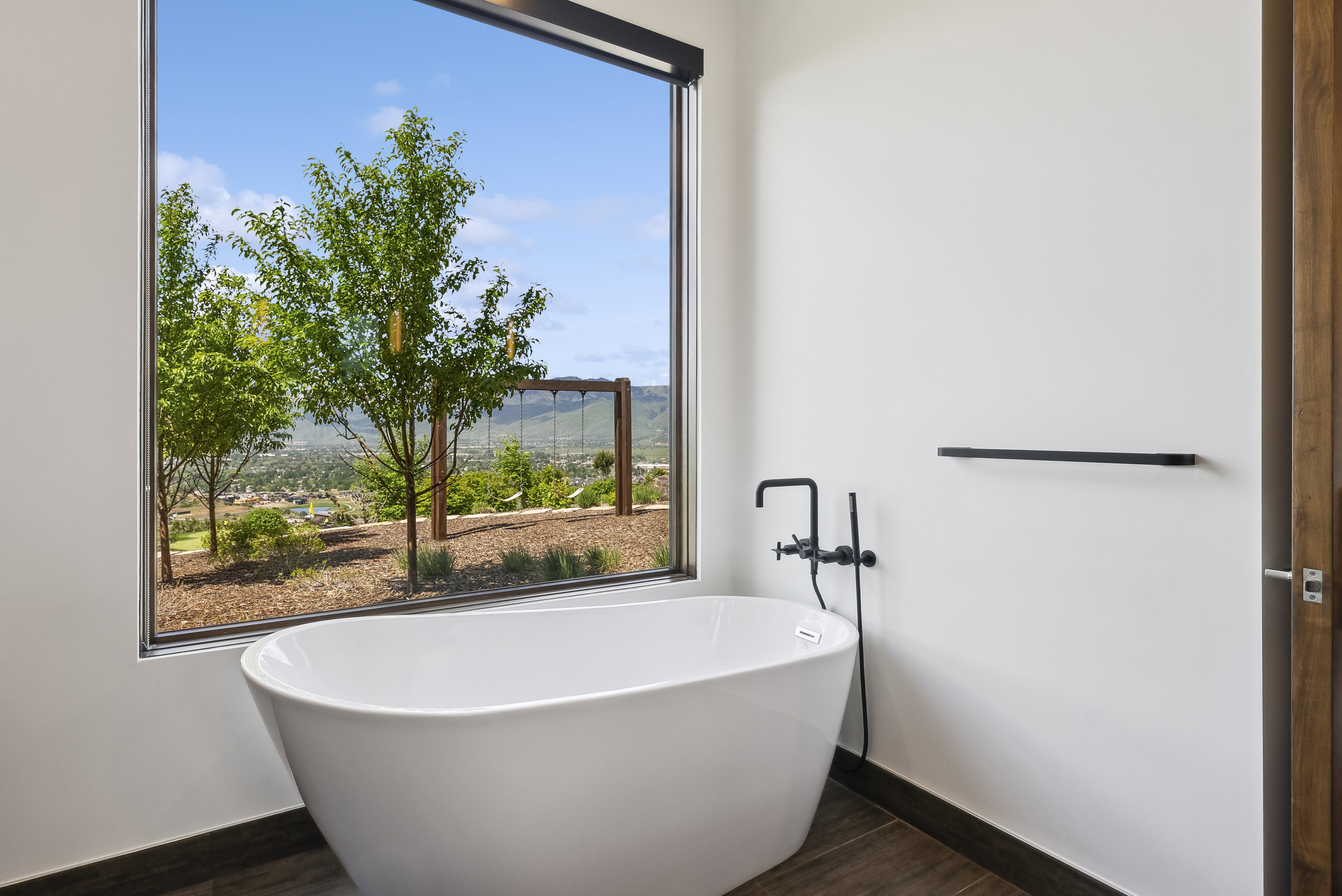 Freestanding soaking tub with matte black fixtures, set against a large picture window