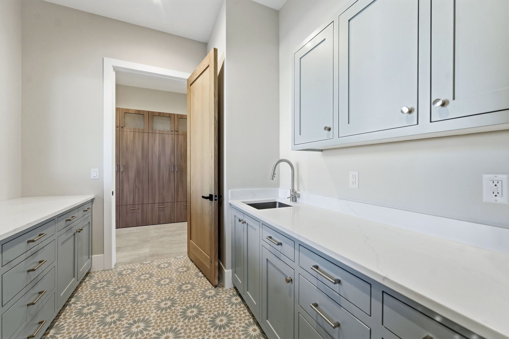 Laundry room featuring patterned tile flooring, light gray cabinetry, white countertops, and a stainless steel sink with a gooseneck faucet