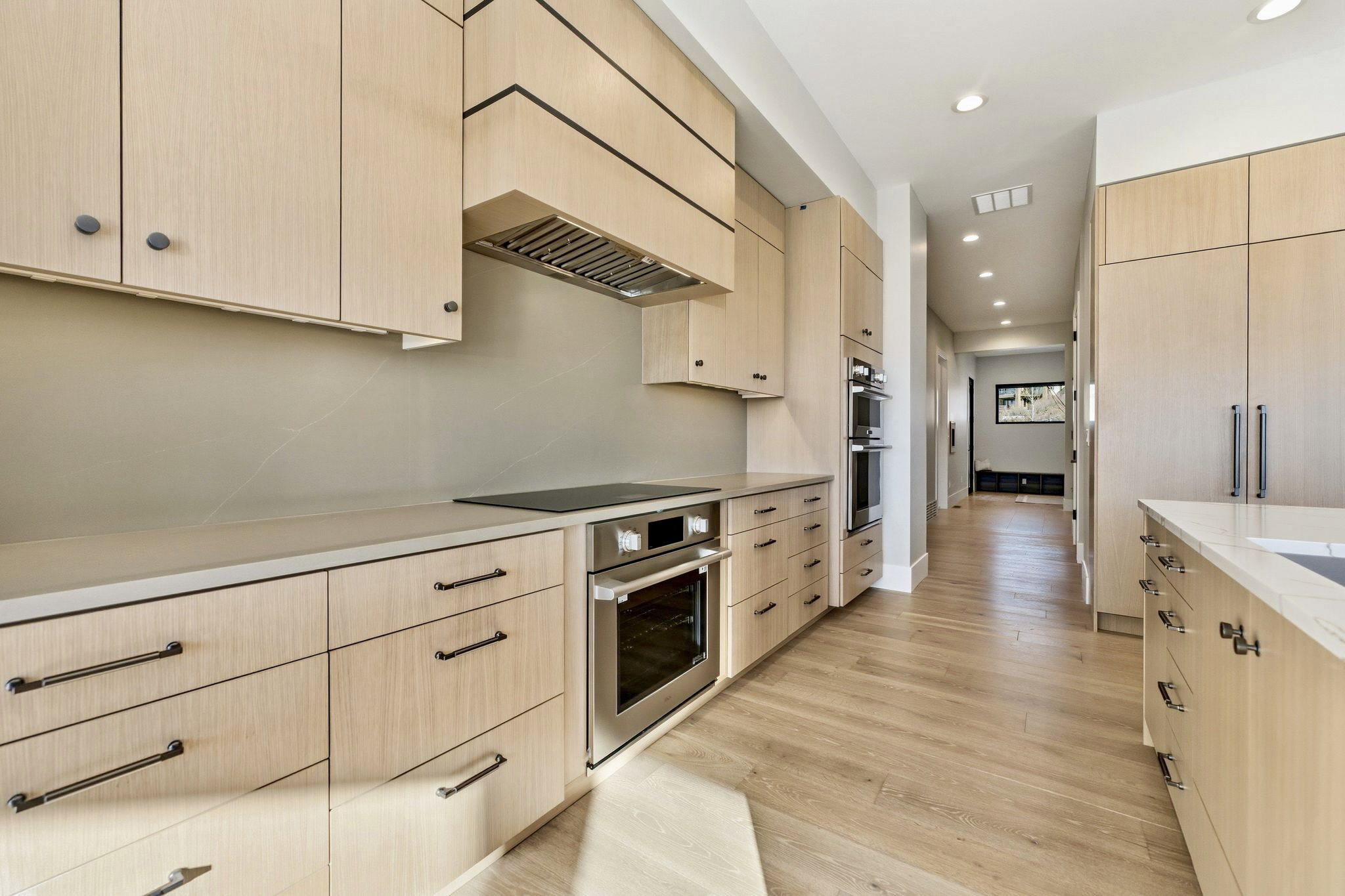 Contemporary kitchen featuring light wood-finish cabinetry with dark hardware, integrated stainless steel appliances, and sleek countertops