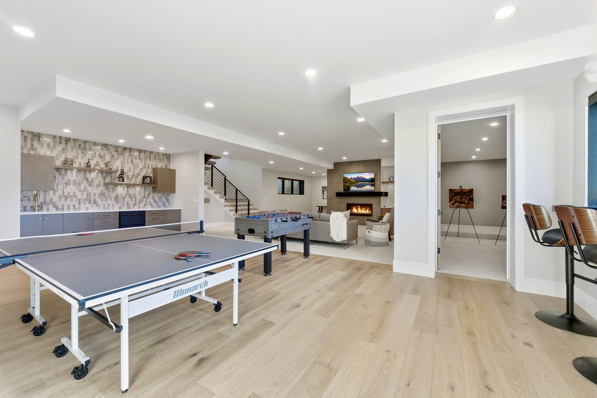 Expansive lower level featuring light wood-finish flooring, recessed lighting, and a built-in wet bar with a tiled accent wall
