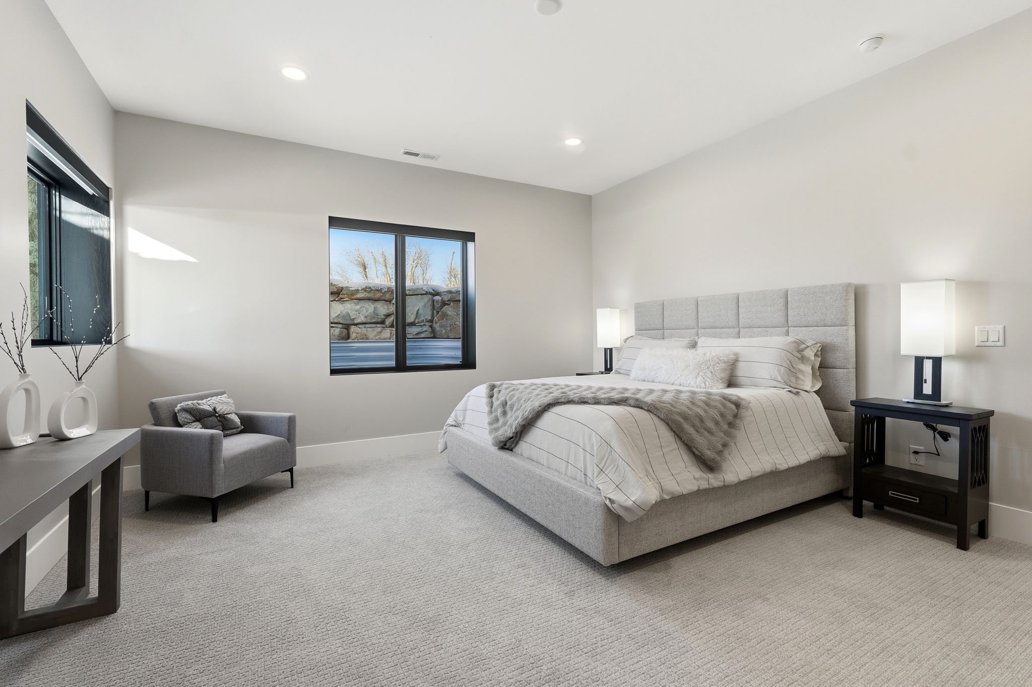 Spacious room featuring light gray walls, plush carpeting, multiple windows with dark frames, and recessed lighting