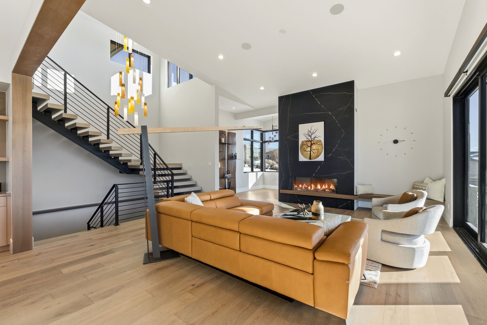 Open-concept living area featuring wood-finish flooring, a modern black stone fireplace, and high ceilings