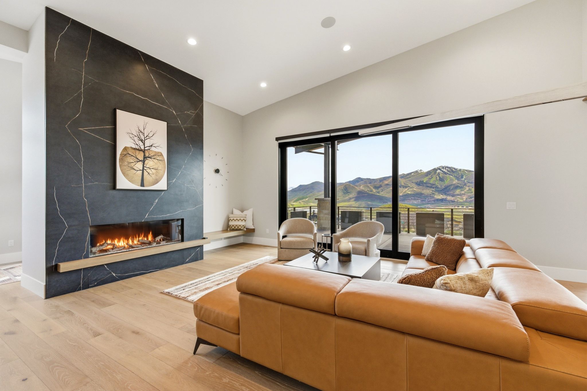 Spacious living area featuring a dramatic floor-to-ceiling fireplace with an extended hearth, wood-finish flooring, and a full wall of sliding glass doors opening to an outdoor patio with mountain scenery