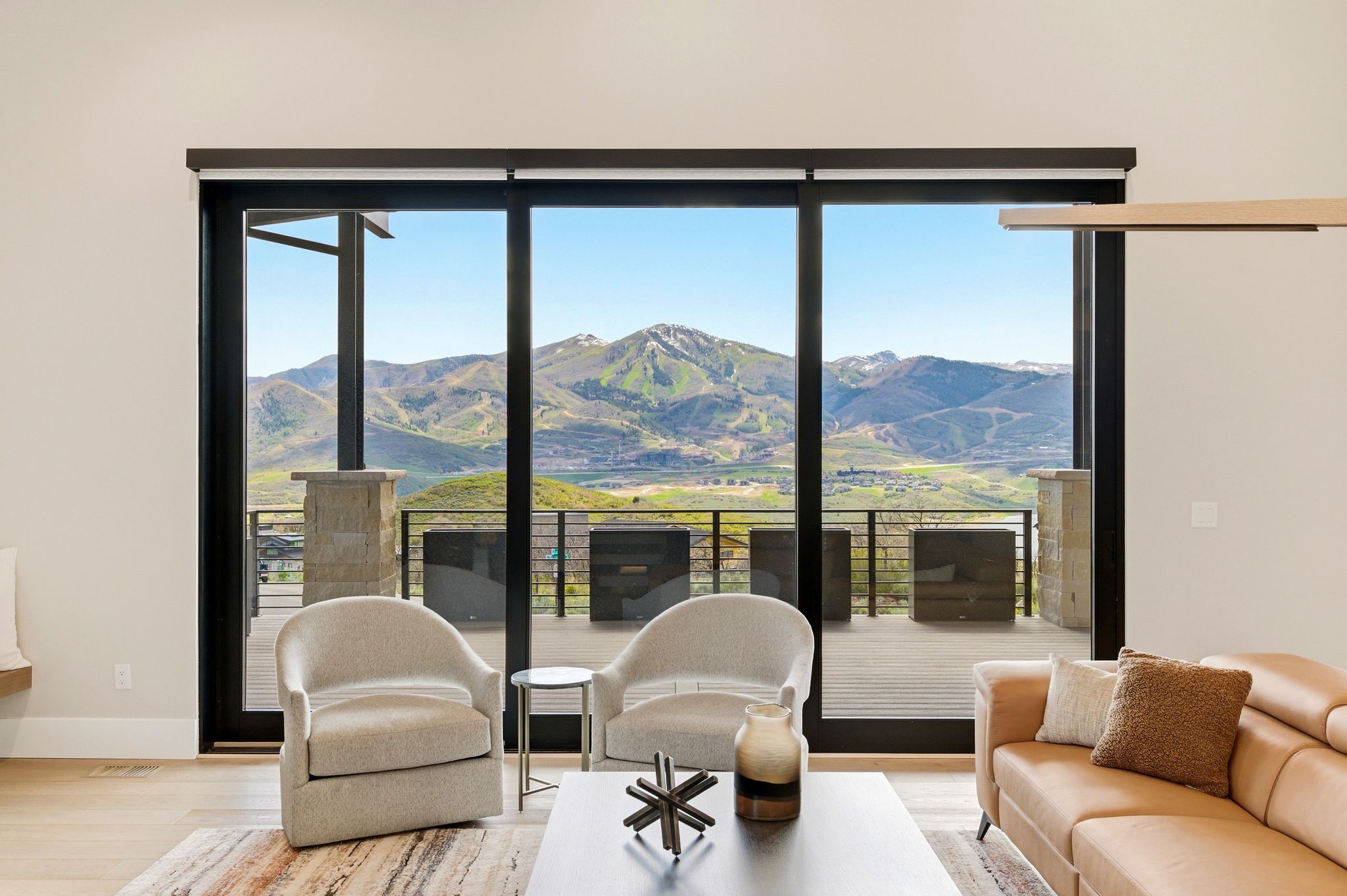 Floor-to-ceiling glass doors opening onto an expansive outdoor deck with mountain scenery