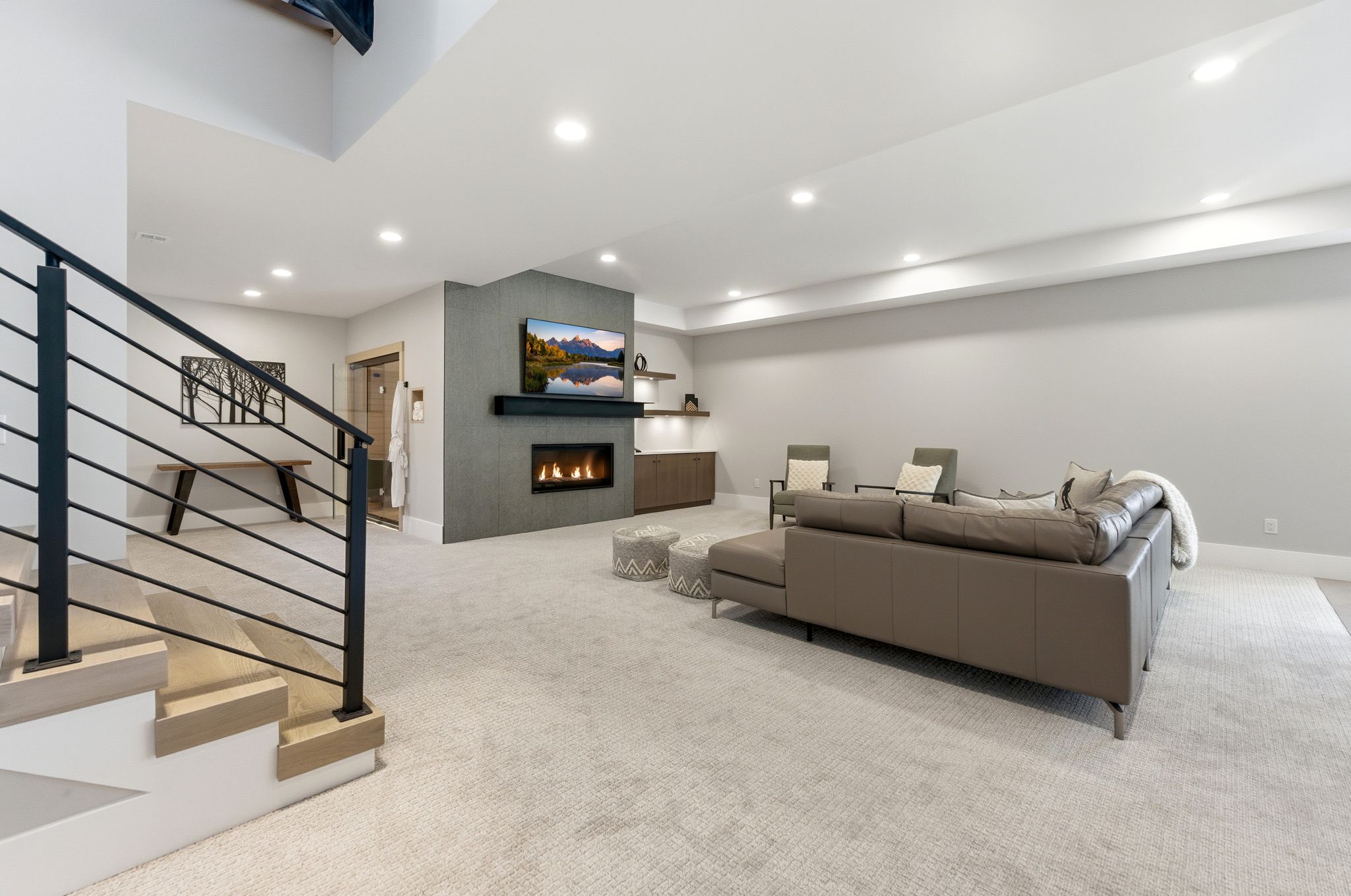 Spacious recreation room featuring a contemporary fireplace with a sleek mantel, recessed lighting, and a modern horizontal railing staircase