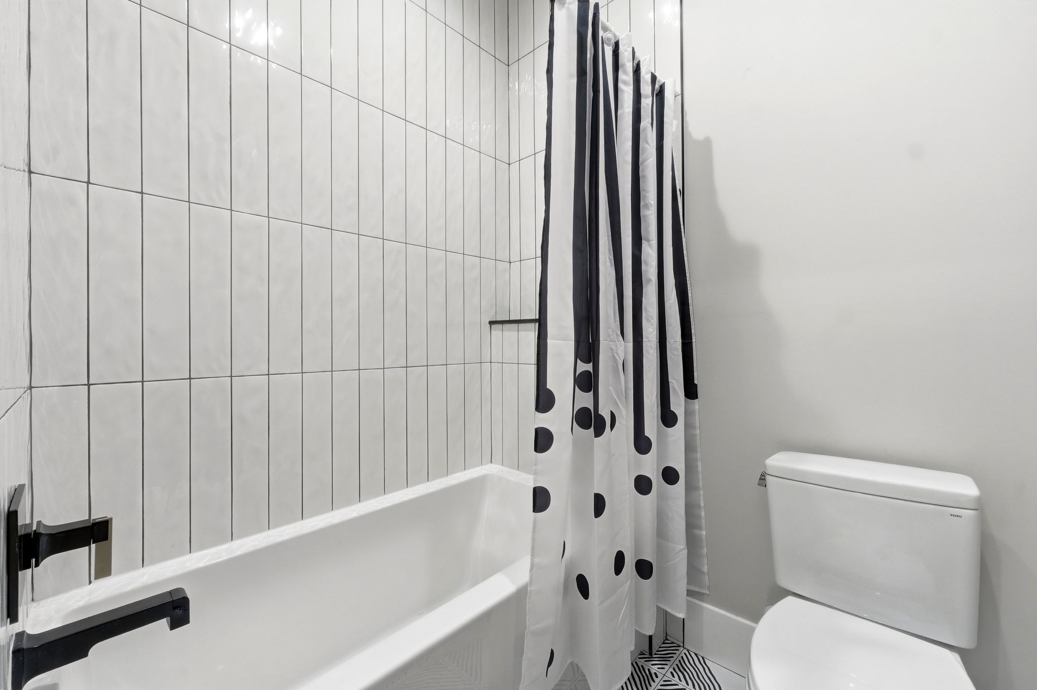 Bathroom featuring a white bathtub, vertical subway tile surround, matte black fixtures, and a white toilet
