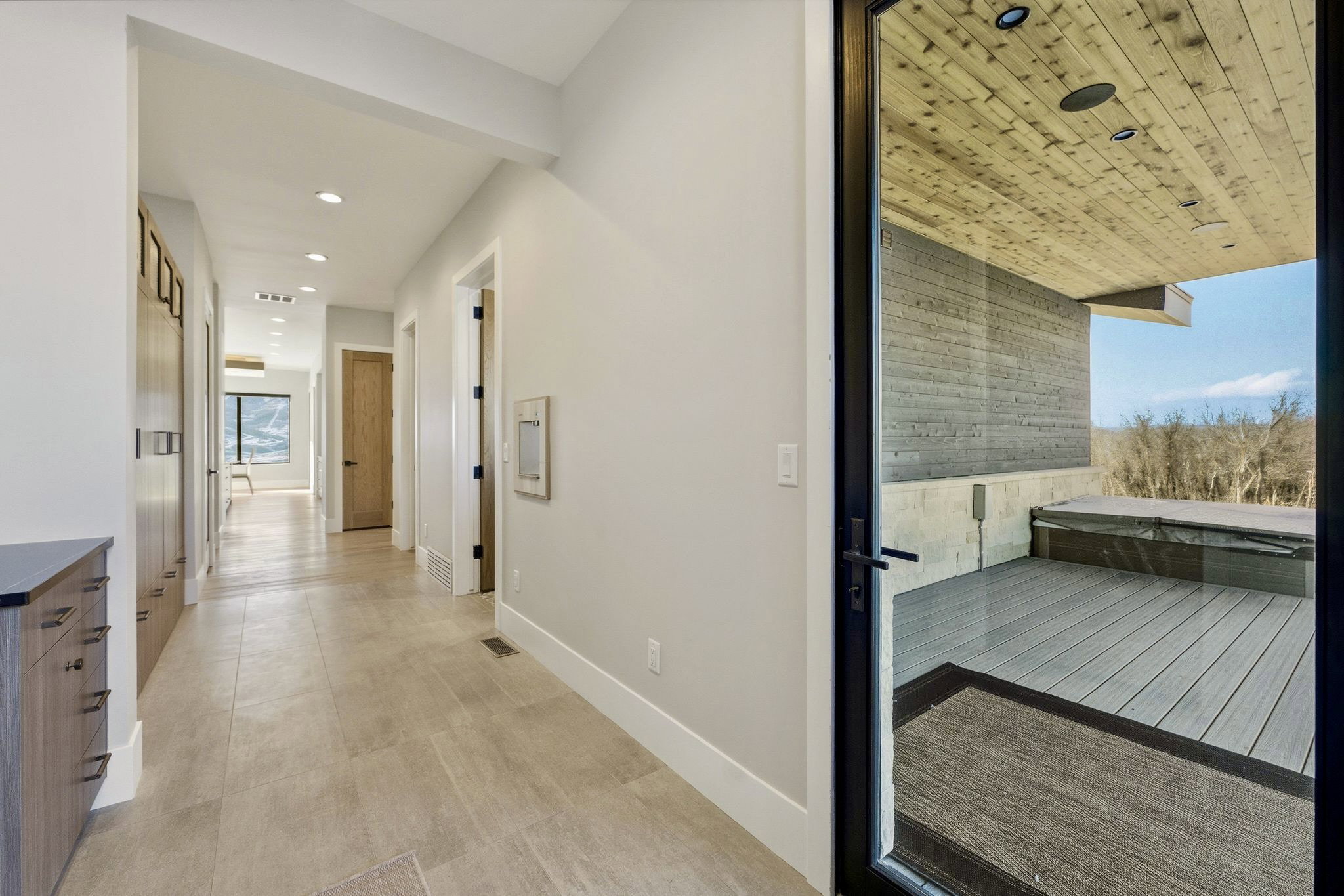 Hallway featuring recessed lighting, light-toned tile flooring, and integrated wood-finish cabinetry with dark hardware