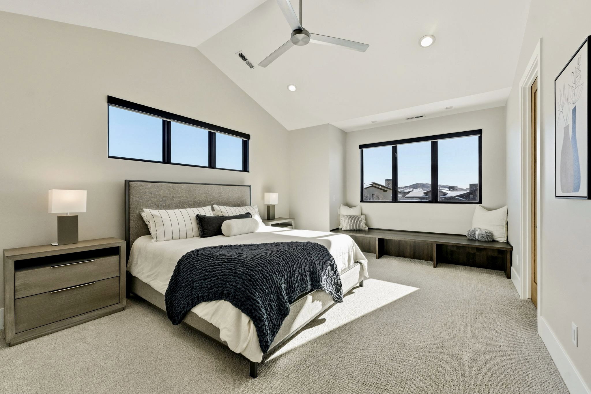 Vaulted ceiling bedroom featuring a contemporary ceiling fan, recessed lighting, expansive windows with black frames, and a built-in window bench