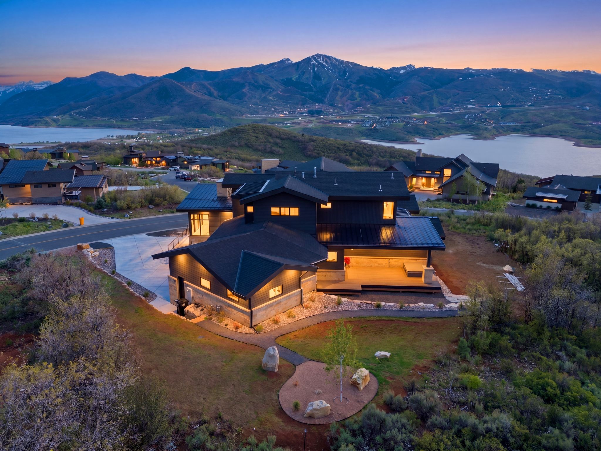 Contemporary mountain home featuring a dark exterior with stone accents, a multi-tiered roofline, and integrated outdoor lighting