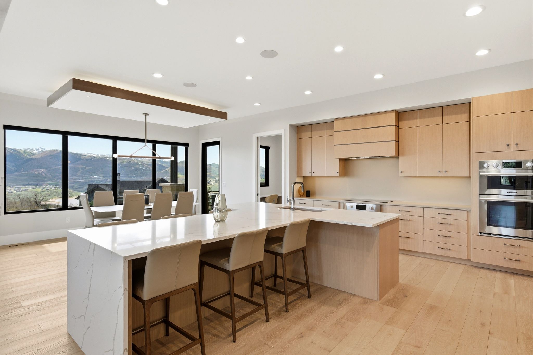 Open-concept kitchen and dining area featuring a waterfall island with seating, integrated appliances, light wood-finish cabinetry, and wide plank wood-finish flooring