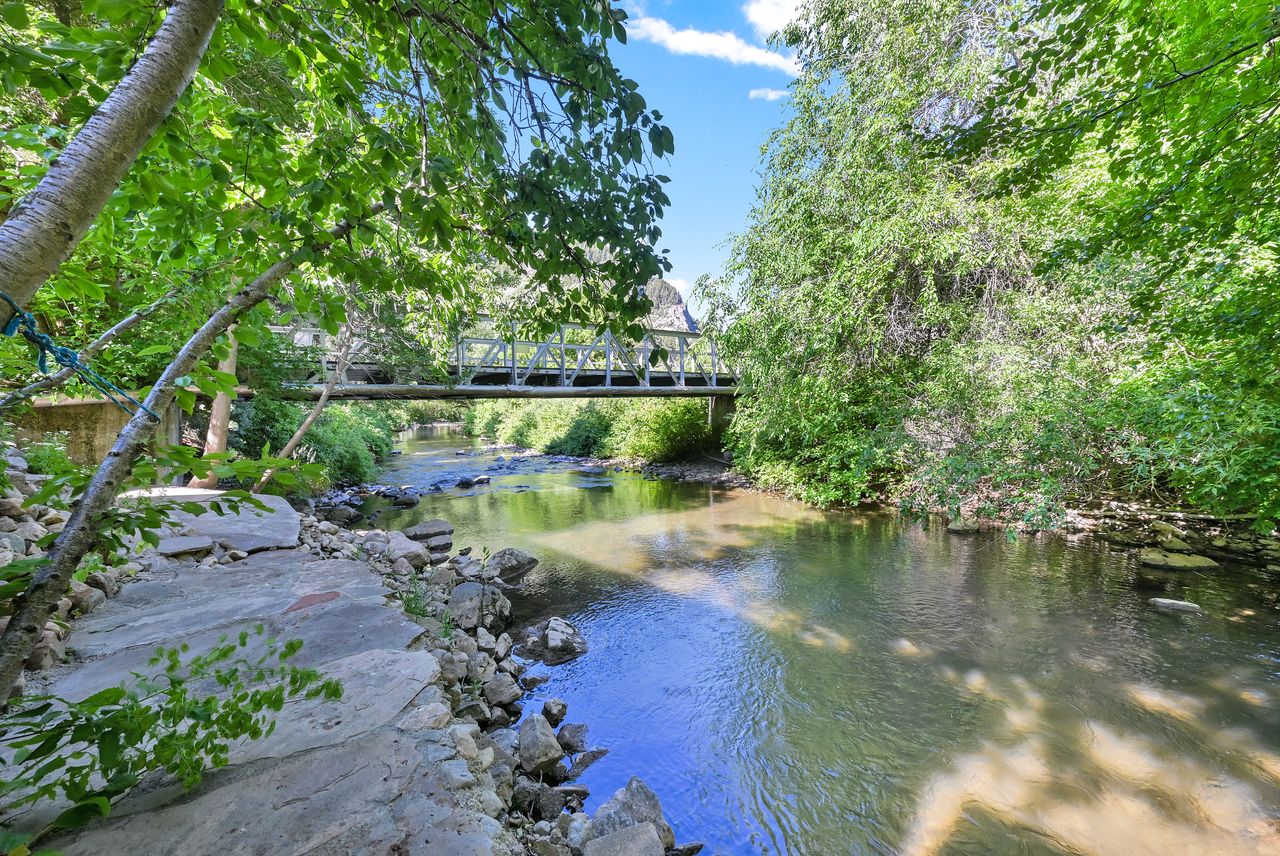 Riverside property featuring a tranquil stream, a footbridge, and abundant natural foliage