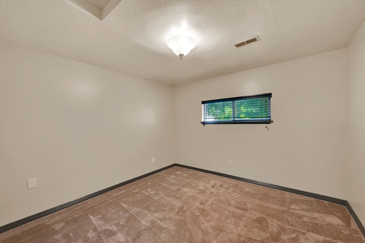 Interior room featuring light-toned walls, a brown carpeted floor, and dark baseboards