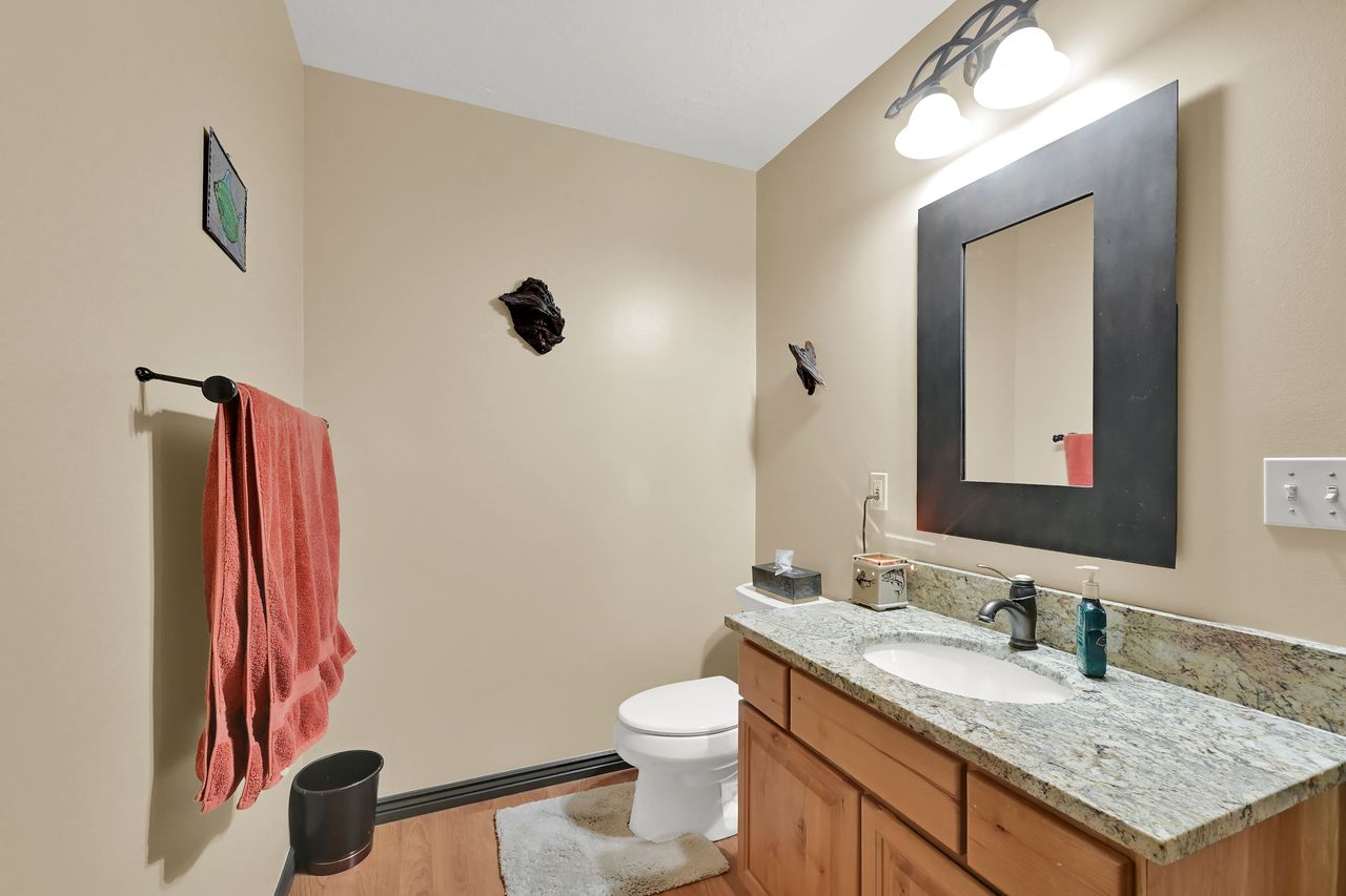 Bathroom featuring a wood-finish vanity with granite-style countertop, undermount sink, and dark hardware