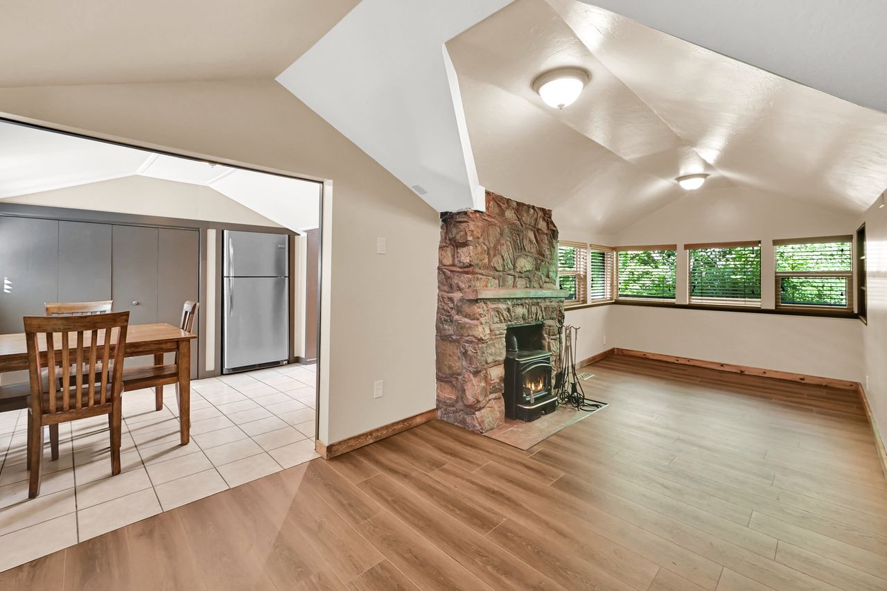 Living area featuring a stone fireplace with a wood-burning stove insert, wood-finish flooring, and multiple windows