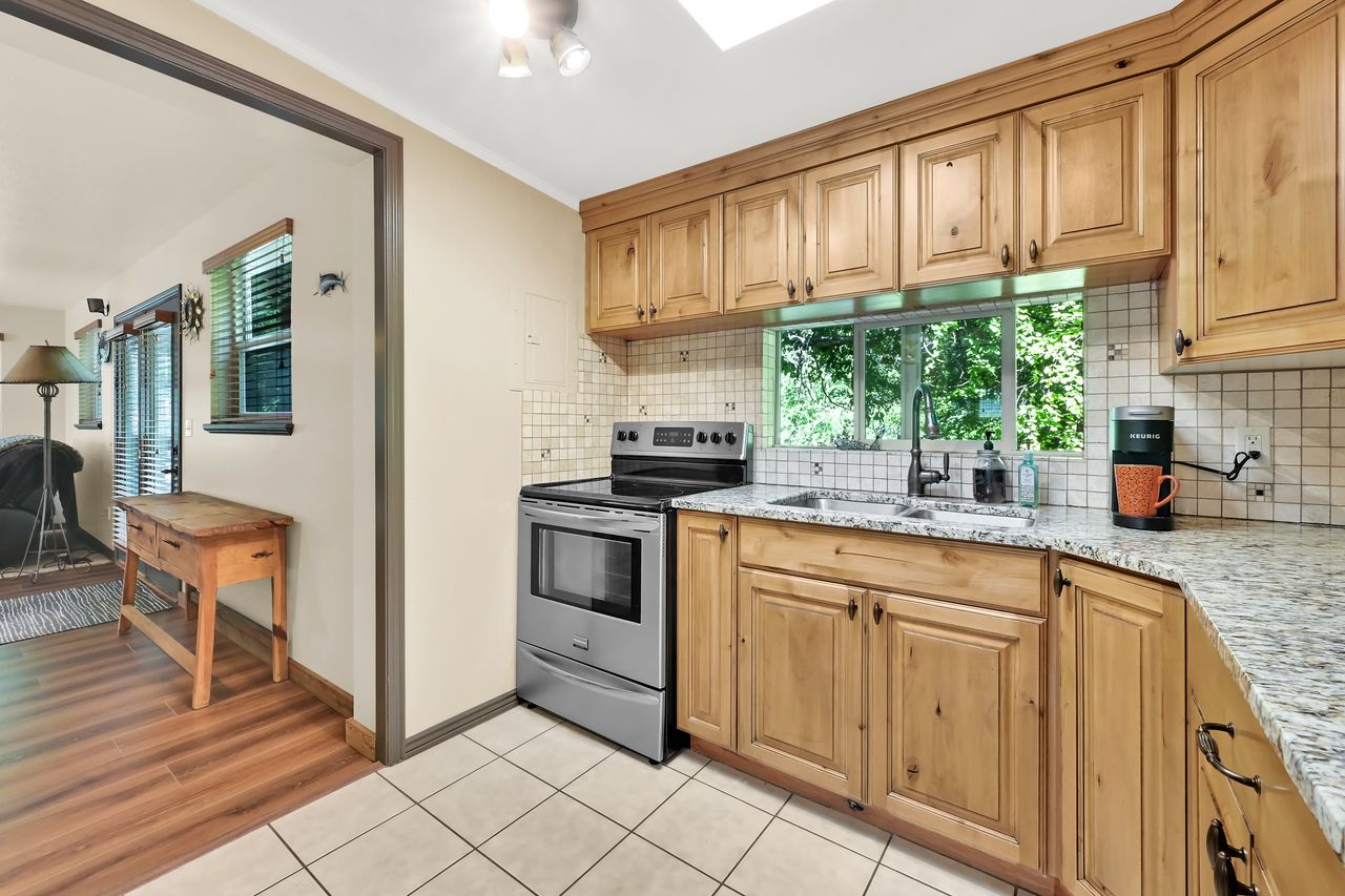 Kitchen featuring light wood cabinetry, stone countertops, stainless steel appliances, a tile backsplash, and a window above the sink