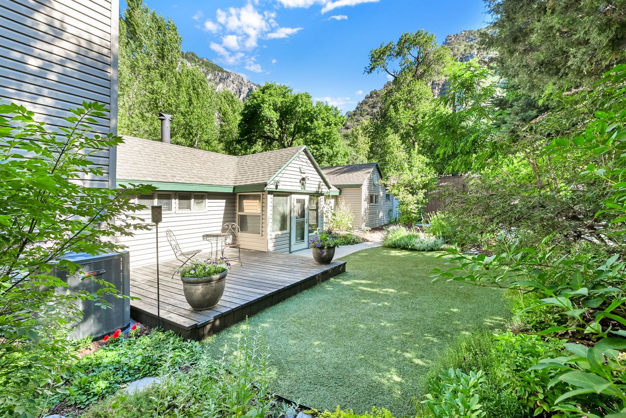 Rear exterior with a wood deck, artificial turf lawn, and surrounding mature foliage