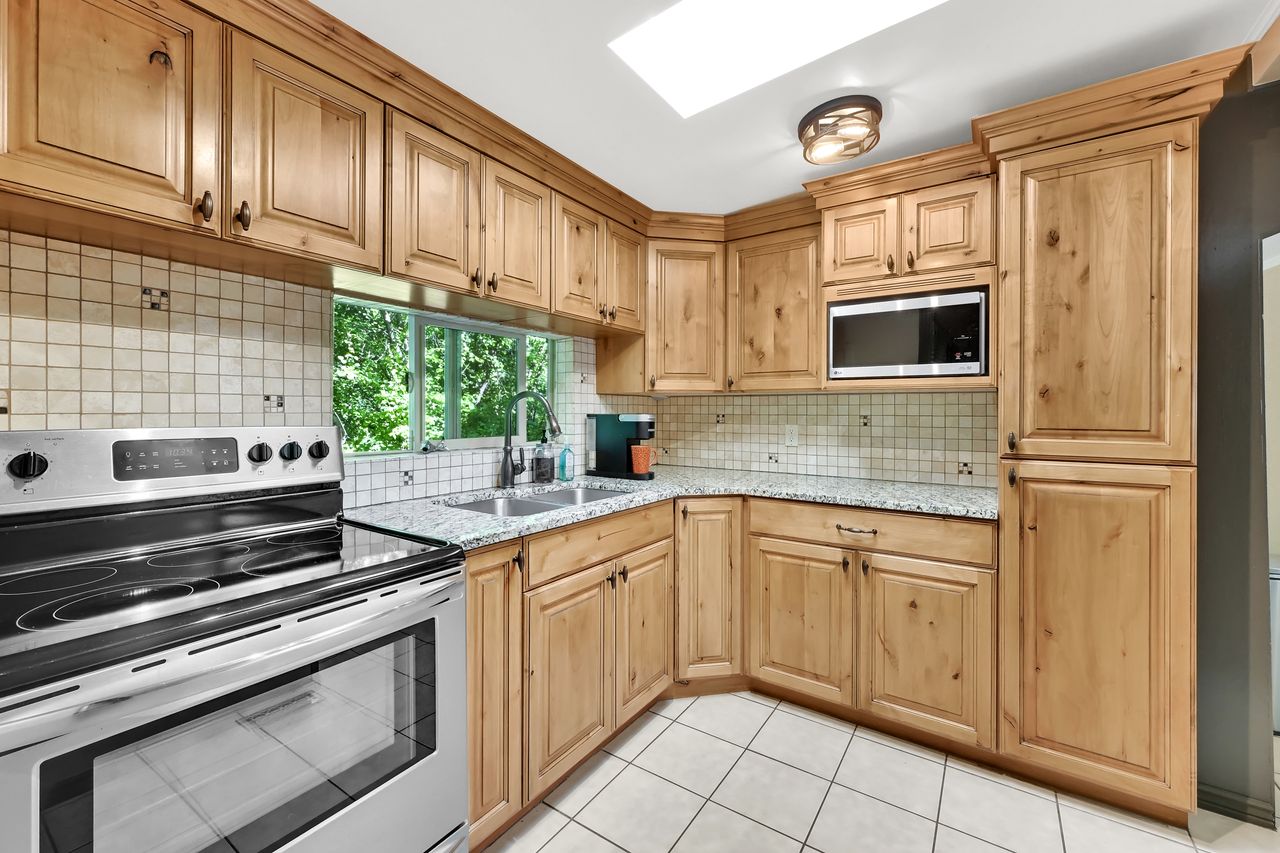 Kitchen featuring wood cabinetry, granite-finish countertops, stainless steel appliances, a tiled backsplash, and a skylight