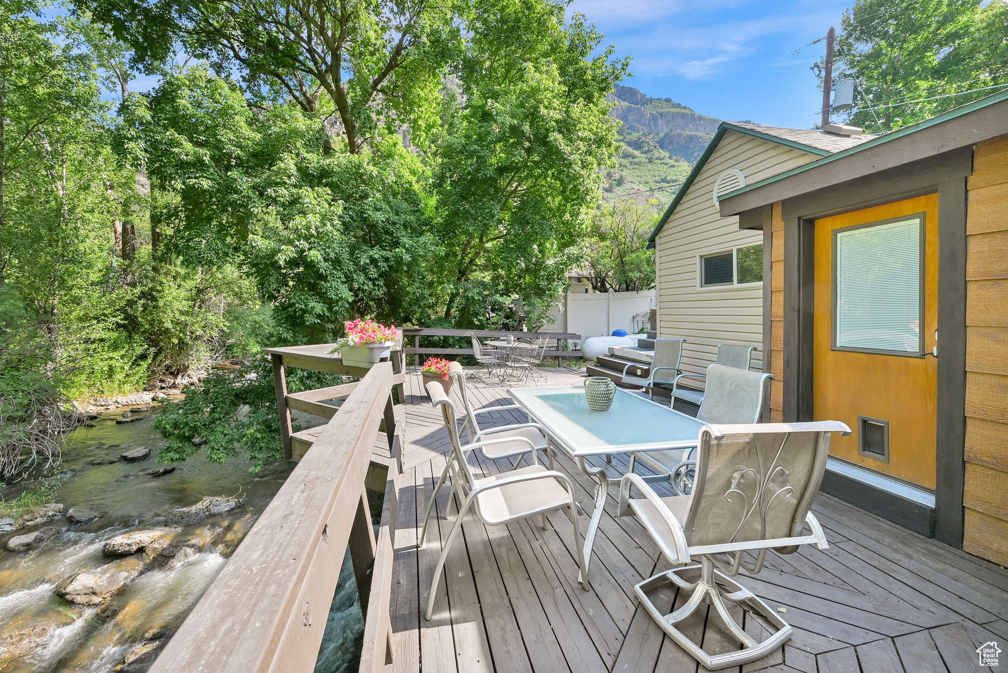 Expansive wood-finish decking featuring a natural water feature, mountain backdrop, and surrounding mature trees
