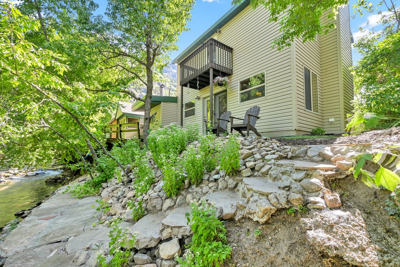 Riverside property featuring a multi-level rock and concrete pathway, a private upper deck, and a lower patio area