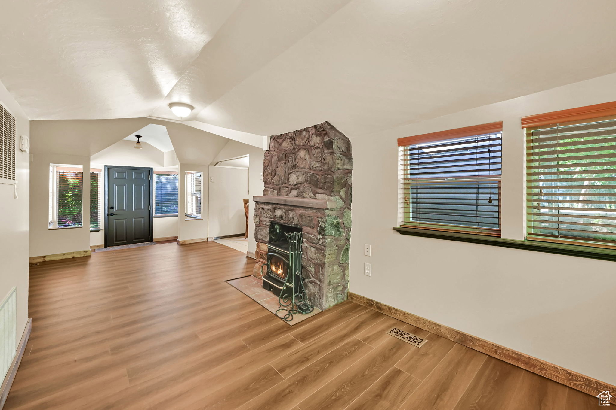 Spacious living area featuring wood-finish flooring, a prominent stone fireplace with a wood-burning stove, and multiple windows