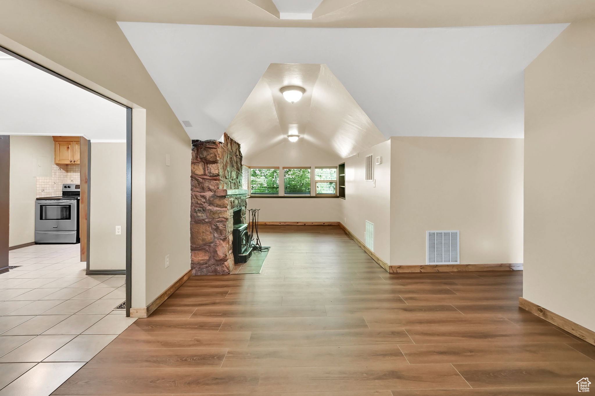 Spacious living area featuring wood-finish flooring, a stone fireplace, and multiple windows providing natural light