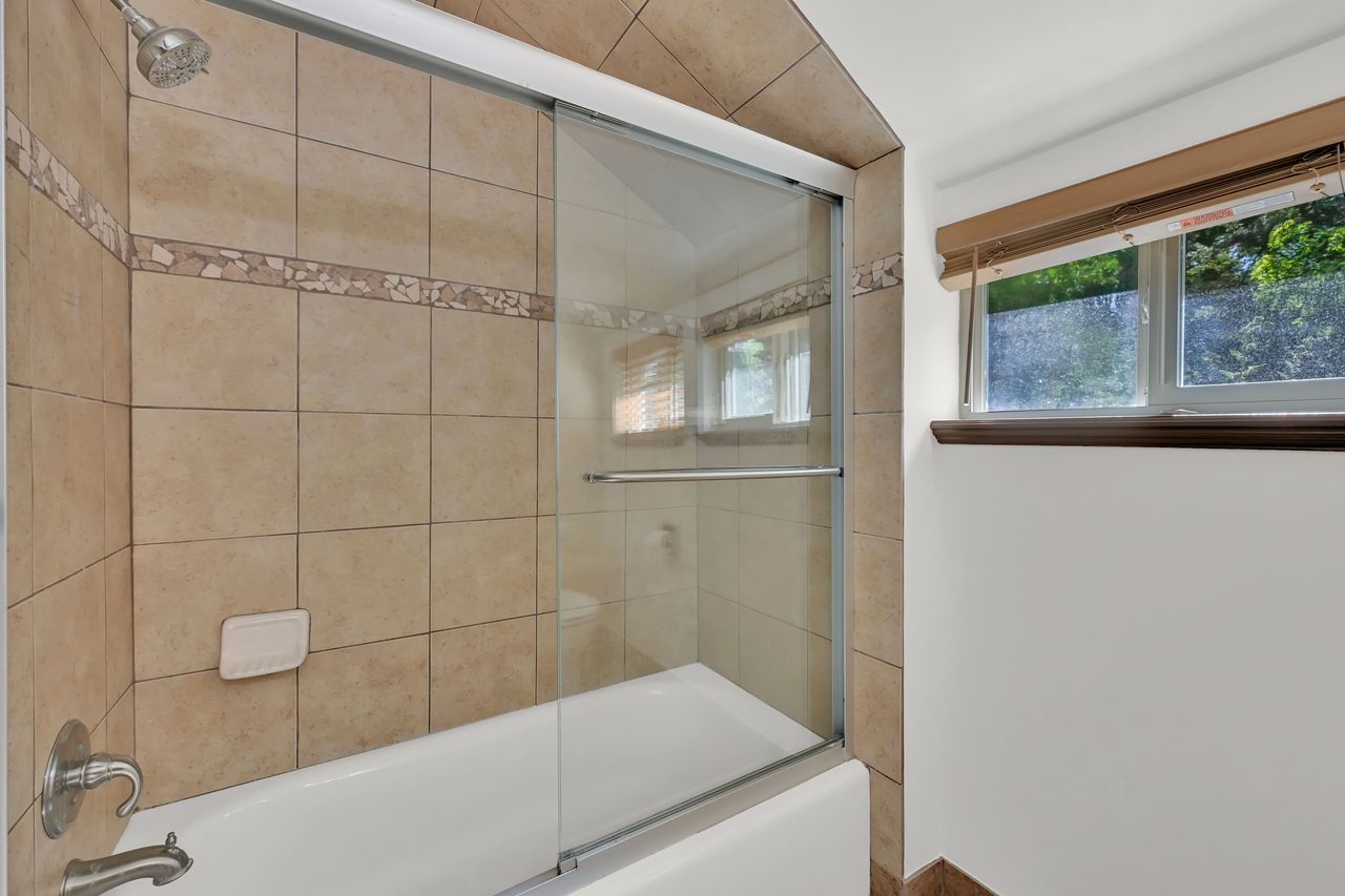 Bathtub with sliding glass shower doors, featuring a tiled surround with decorative accent banding
