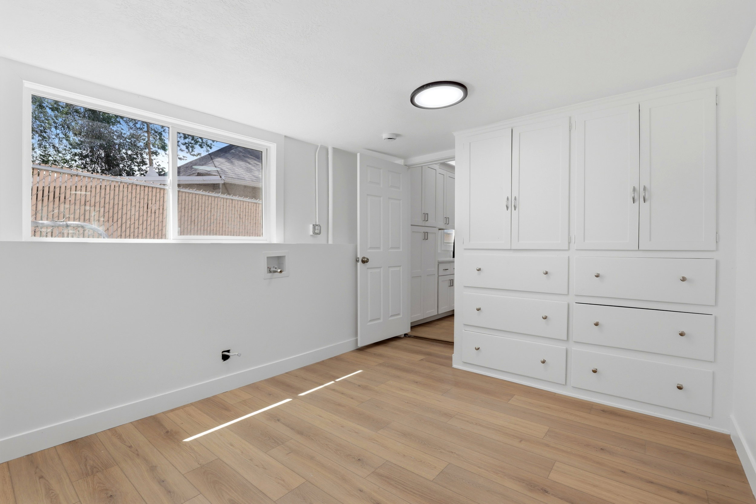Bright utility space featuring light wood-finish flooring, a window, and built-in white cabinetry with drawers