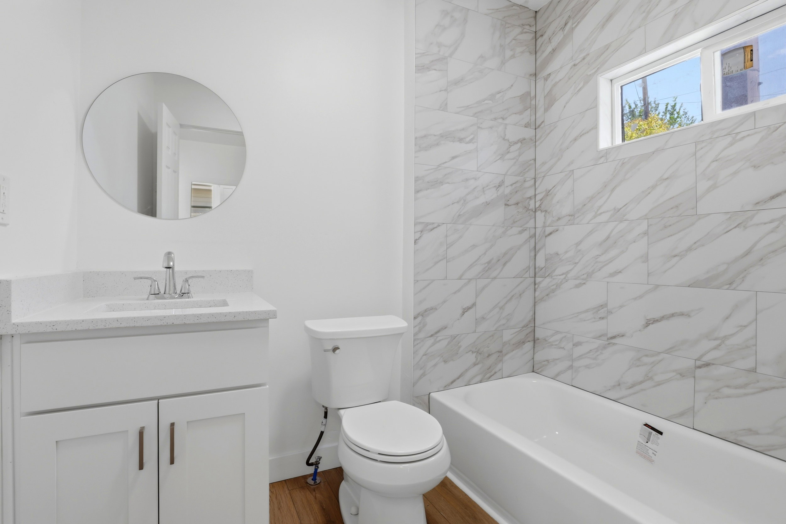Contemporary bathroom featuring a white vanity with quartz countertop, chrome faucet, and a round frameless mirror